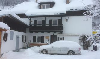 A snow-covered house with a balcony and a snow-covered car. The surroundings are wintry and calm.