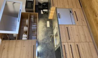 A modern kitchen with wooden cabinets and gray countertops. It includes a sink, a dishwasher, and a microwave.