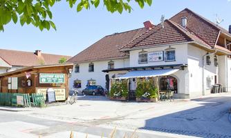 A traditional inn with an inviting entrance and a green outdoor seating area. Surrounded by trees and a blue sky, the atmosphere feels friendly and welcoming.