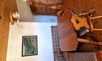 A cozy dining area with a wooden table and a bench. A picture hangs on the wall, and there is an antique cabinet in the corner.