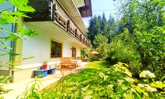 A cozy house with a balcony and a well-maintained garden. Surrounded by trees and green plants, the scene radiates tranquility and a connection to nature.
