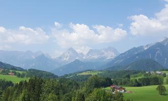 A picturesque mountain landscape with green meadows and impressive peaks. The sky is blue with some clouds.