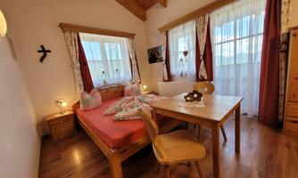 A cozy bedroom with a double bed and a table. Large windows bring a lot of light into the room.