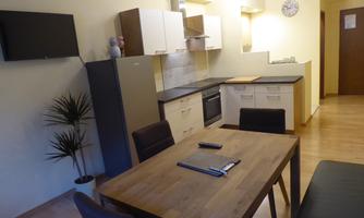 A modern kitchen with a wooden table and chairs. In the background, a refrigerator and a sink are visible.
