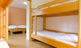 A simple room with a wooden bunk bed and a double bed. The room feels bright and inviting.