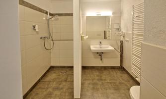 A modern bathroom with a shower, a sink, and large tiles. The walls are bright and there is plenty of light.