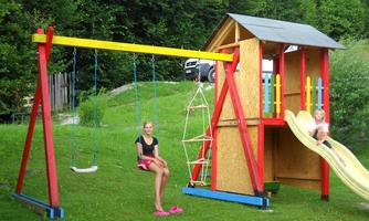 A playground with a colorful climbing frame, a slide, and swings. Two girls are happily playing in the greenery.