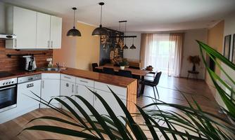 A modern kitchen with an open living area. There is a large dining table and plenty of natural light.