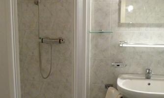 A bathroom with a shower and a white sink. The walls are tiled and the fixtures are simple and functional.