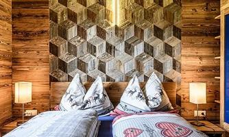 A cozy bedroom with two beds and a decorative wall made of wooden panels. The lighting creates a warm and inviting atmosphere.