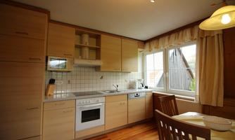 A modern kitchen with wooden cabinets and a large window. The dining area is cozy with a table and chairs set up.