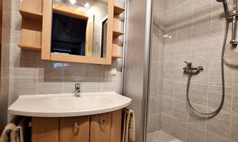 A modern bathroom with a shower and a suspended mirror. The sink with wooden cabinets provides additional storage space.