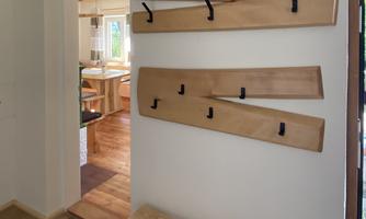 A modern entrance area with wooden slats on the wall that provide hooks for hanging. A bright, friendly atmosphere can be seen with a view into the next room.