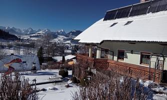 A beautiful house in the snow with a clear blue sky. The surrounding mountains are clearly visible and the landscape is wintery idyllic.