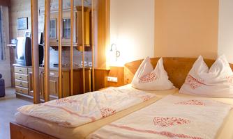 A cozy bedroom with two single beds and red accents. In the background, wooden furniture and a television are visible.
