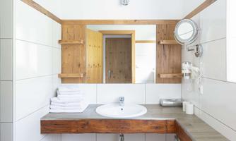 A modern bathroom with a sink and a large mirror. Towels and wooden shelves give the space a cozy atmosphere.