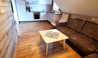 A cozy living area with a sofa and a table. Modern appliances are visible in the kitchen.