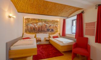 A modern furnished bedroom with two beds and a red carpet. A large wall mural depicts a group of foxes in nature.