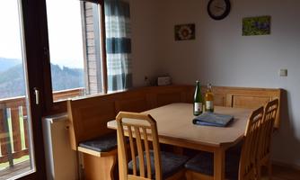 A cozy dining area with a wooden table and chairs. The large window front offers a beautiful view of the mountains.