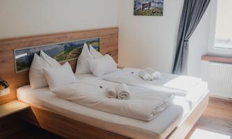 A cozy bedroom with a double bed and two pillows. The room has large windows and minimalistic decoration.