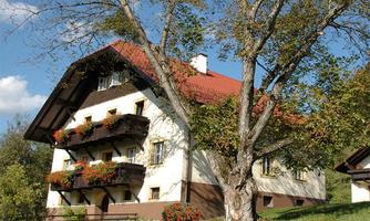 A charming house with a red roof and blooming balconies. Surrounded by green grass and trees outside.