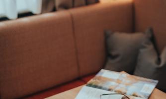 A cozy spot with a cup of coffee on a wooden table. In the background, there is a magazine and a small plant.