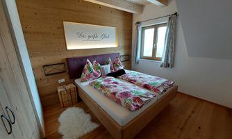 A cozy bedroom with a wooden wall design and a large bed. Colorful pillows and a window view create an inviting atmosphere.