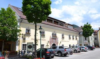 A charming building with traditional architecture and colorful flowers. Parked cars and bicycles can be seen in front of the house.