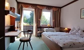 A cozy hotel room with two single beds, a desk and chairs. Large windows offer a view of the greenery.