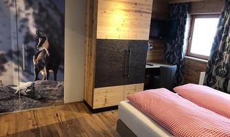 A cozy bedroom with a double bed and red-and-white checked pillows. The wardrobe features an impressive mountain landscape on the door.
