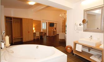A modern bathroom with a round bathtub and an elegant sink. In the background, wooden cabinets and a television are visible.