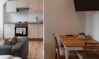 A modern kitchen with wooden shelves and a dining table. The living area is bright and cheerfully furnished.