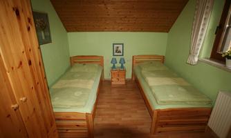 A simple bedroom with two single beds and a green wall. There is a nightstand and a window with curtains, as well as a picture on the wall.