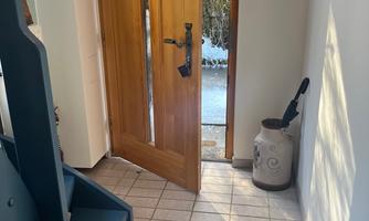 An inviting entrance area with an open wooden door and a large green rug. Against the wall are a blue shelf and a container.
