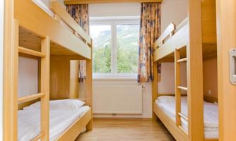 A simple room with two bunk beds and a window. The room has bright walls and a wooden floor.