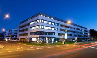 A modern office building at night, illuminated by streetlights. In the foreground, a traffic road with road markings is visible.