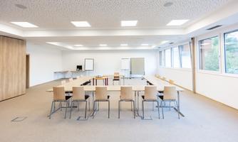 A bright meeting room with a large table and chairs. The windows provide a view of the nature outside.