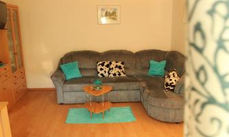 A cozy living room with a gray sofa and colorful cushions. A round table and a turquoise rug complete the decor.