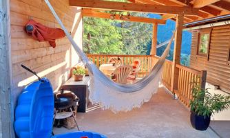 A cozy outdoor area with a hammock and a blue sandbox. The space is surrounded by wood and offers a view of the green surroundings.