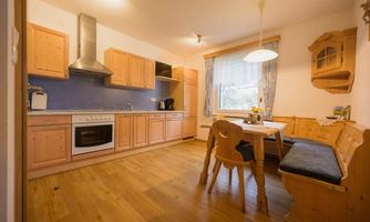 A cozy kitchen with wooden furniture and a bright atmosphere. The table is set for several people and there is a stove and a sink.