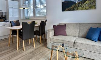 A modern living room with a comfortable couch and a dining table. In the background, there is a picture of mountains and green hills.