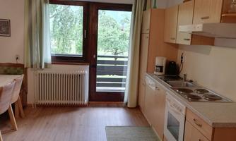 A bright kitchen with a dining table and a balcony. The equipment includes hotplates, a refrigerator, and a kettle.