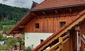 A traditional wooden house with a sloped roof. In the background, there are wooded hills and a gray sky.