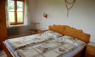 A cozy bedroom with a double bed and wooden furniture. There is a window overlooking the greenery and a decoration on the wall.