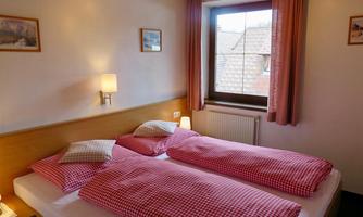 A cozy bedroom with two single beds. The walls are painted light and there are windows with curtains.