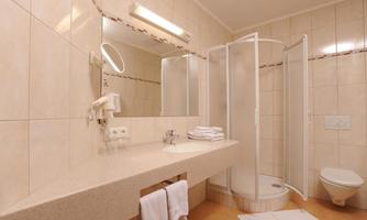 A modern bathroom with a shower and a sink. The walls are brightly tiled and there are fresh towels.