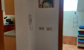 A bright hallway with a wooden piece of furniture and a picture rail on the wall. In the background, an open bathroom with colorful towels can be seen.