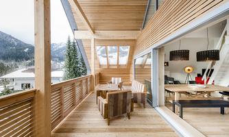 A modern wooden terrace with cozy seating options. In the background, mountains and a clear view of the living area are visible.