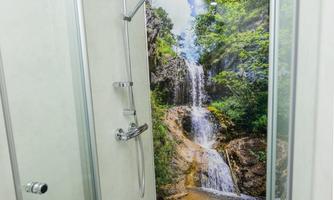 A modern shower with glass walls and a nature wallpaper depicting a waterfall. The space feels inviting and harmonious.