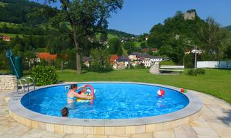 A swimming pool in a beautiful landscape with a child playing. In the background, green hills and a small town can be seen.